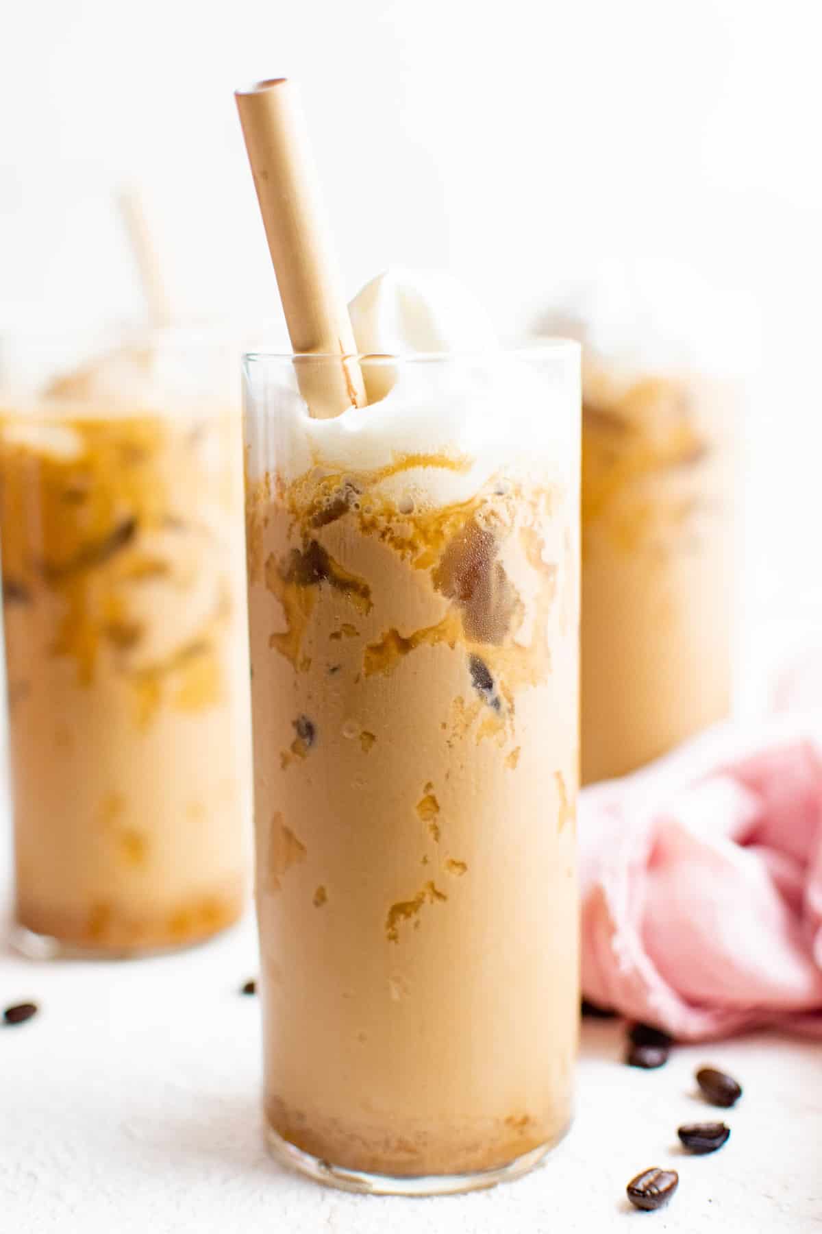 Iced latte, topped with whipped cream, in a tall glass with a brown straw.