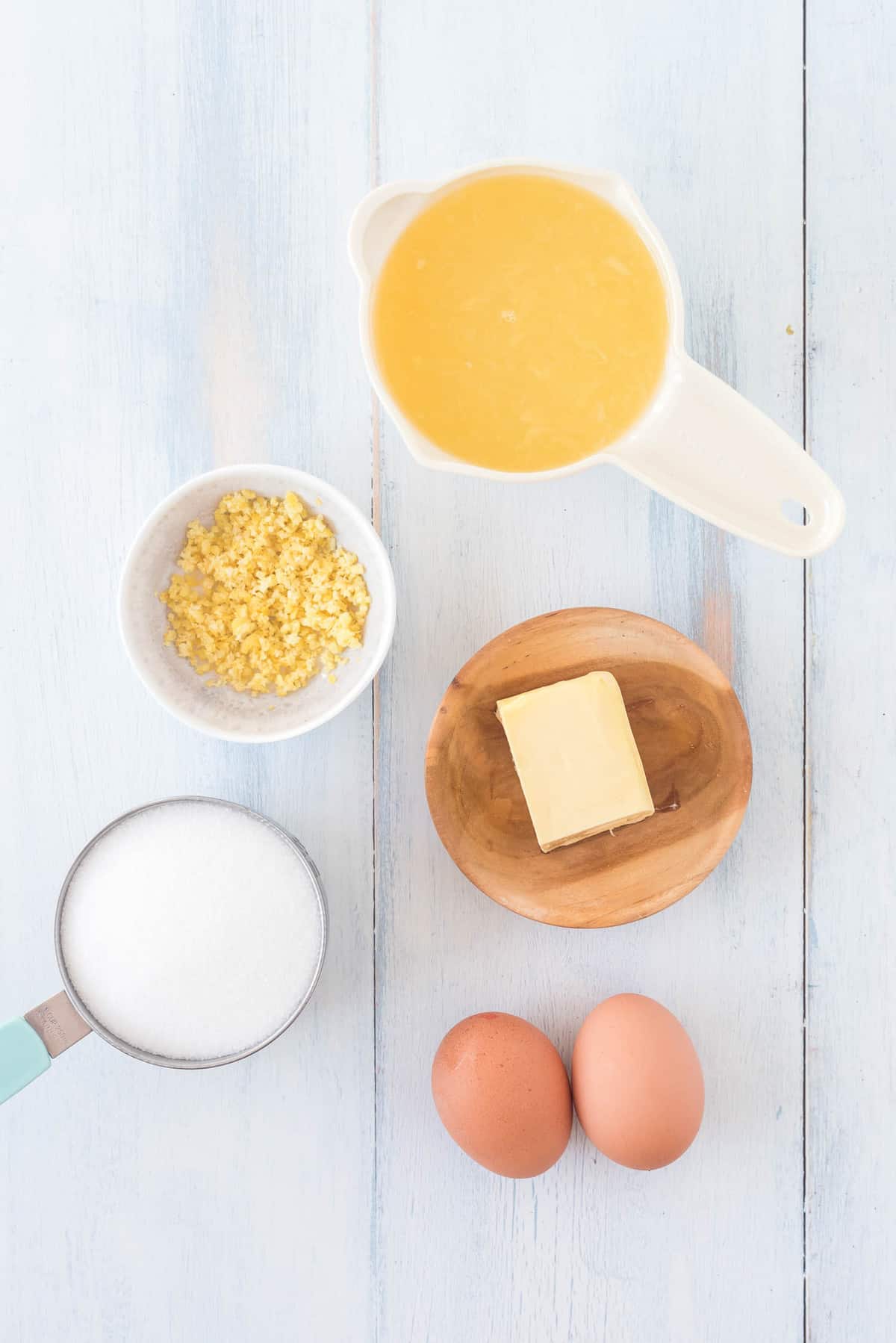 Overhead view of ingredients needed: butter, sugar, lemon juice, lemon zest, eggs.