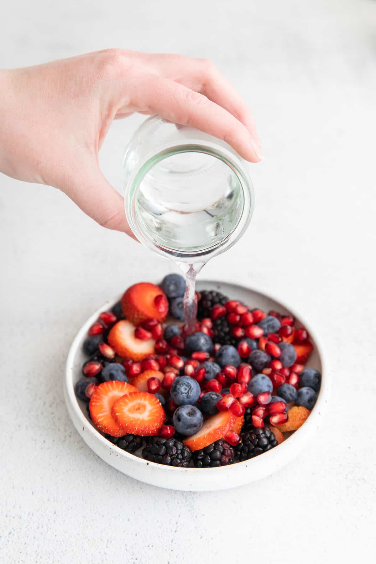 Coconut water being poured into a bowl full of fresh fruit.