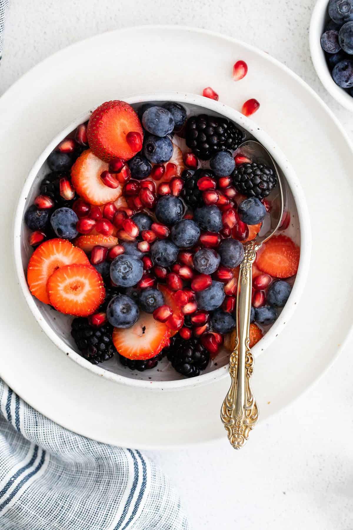 Fresh berries and pomegranates in a bowl with coconut water and a spoon.