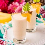 Two tall glasses full of light yellow smoothie, garnished with fresh pineapple.