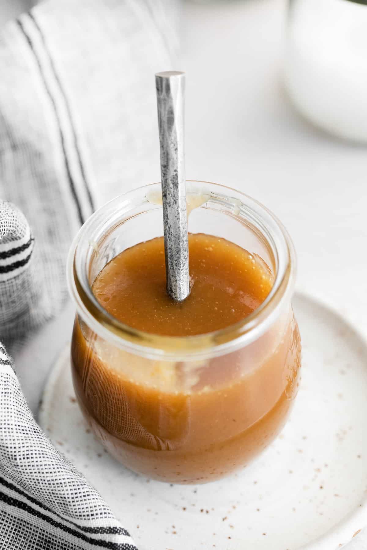 Caramel in a small glass jar with a silver spoon.