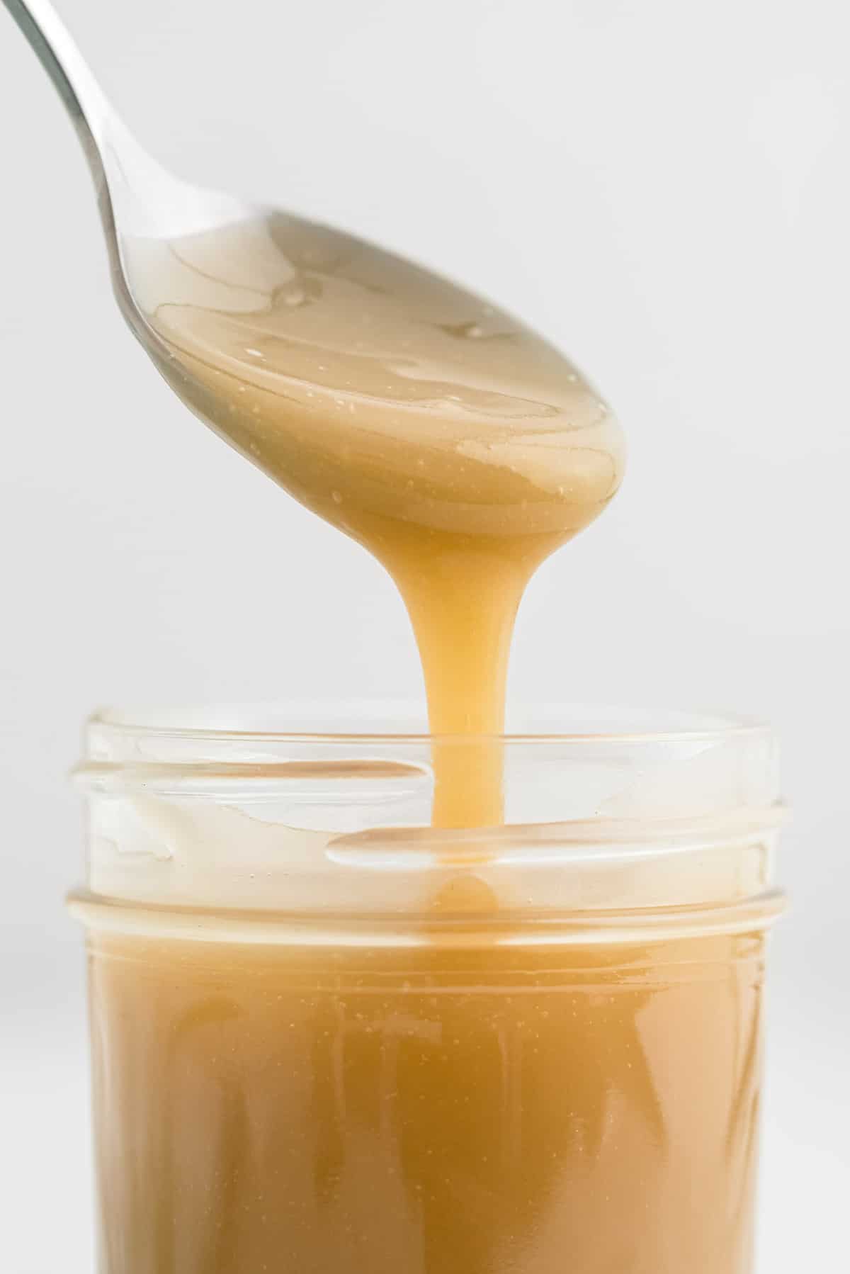 Close up of caramel dripping off a spoon into a jar.
