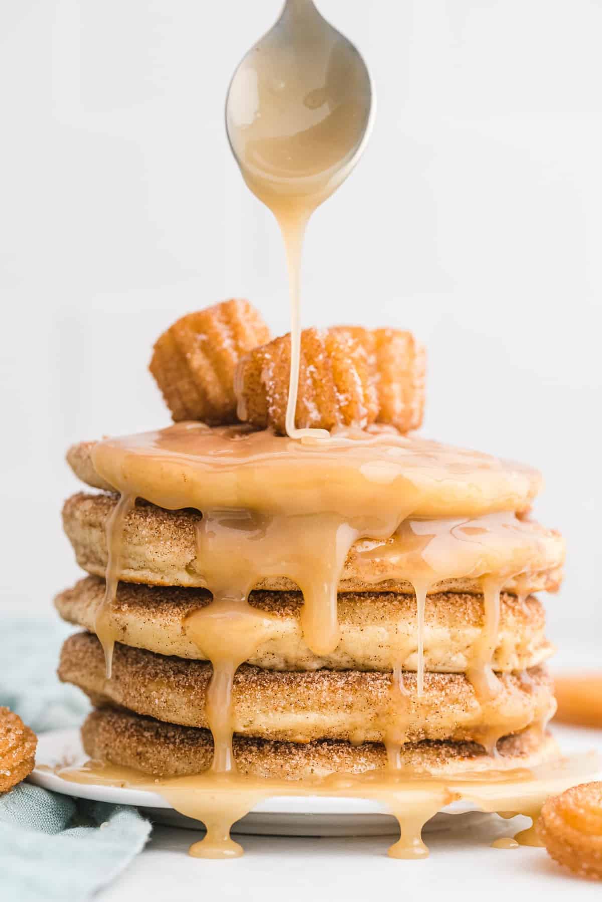 Stack of churro pancakes with caramel being drizzled on them.