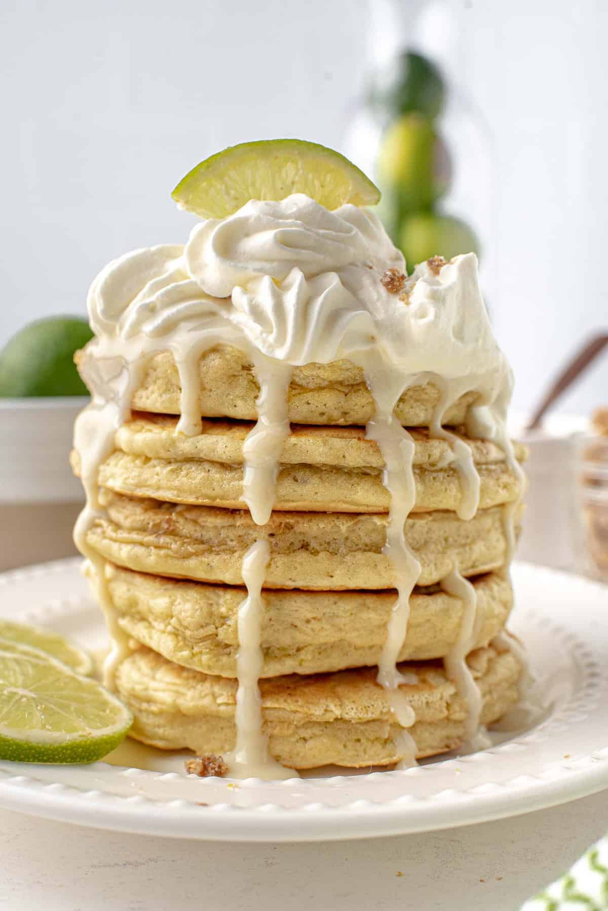 Tall stack of pancakes topped with whipped cream and dripping with lime syrup.