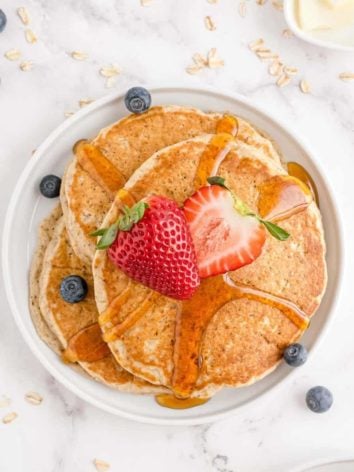 3 pancakes on a white plate, topped with syrup and fresh berries.