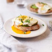 Avocado and runny egg on a slice of toast on a white plate.