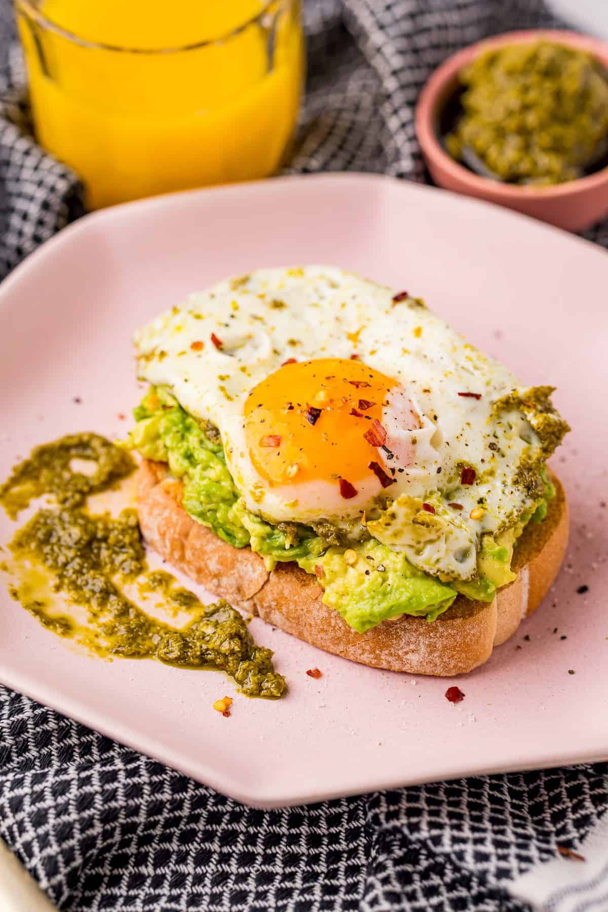 Cooked egg with pesto on avocado toast on a pink plate.