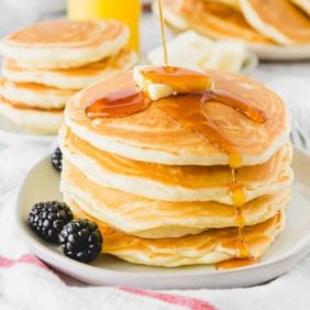 Syrup being poured on a stack of fluffy pancakes.