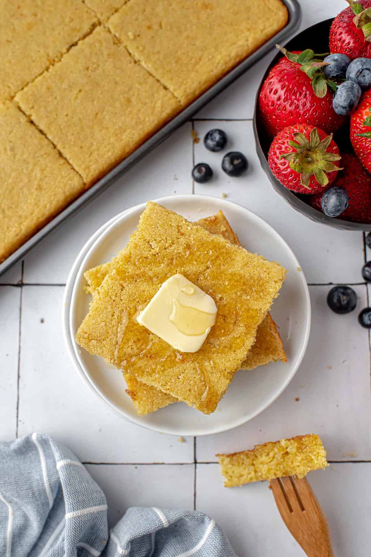 Square gluten-free sheet pan pancakes with butter, fruit nearby.