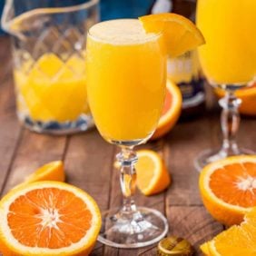 Orange drink in a stemmed glass made with beer and orange juice, topped with orange wedge.