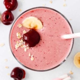 Overhead view of light pink cherry smoothie topped with a cherry, banana slice, and oats.