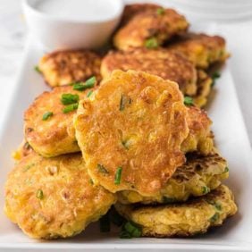 Corn fritters piled high on a white rectangular plate.