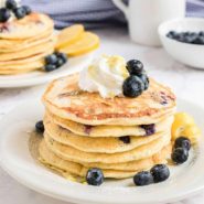 Stack of pancakes topped with whipped cream and blueberries.