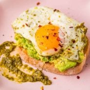 Pesto egg on top of avocado toast on a pink plate.
