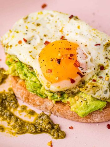 Pesto egg on top of avocado toast on a pink plate.