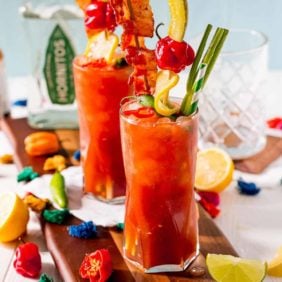 Two bloody maria cocktails garnished with celery, pickles, bacon and more.