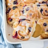 Blueberry roll being taken out of a white casserole dish.