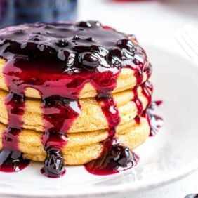 Stack of pancakes with blueberry sauce dripping down it.