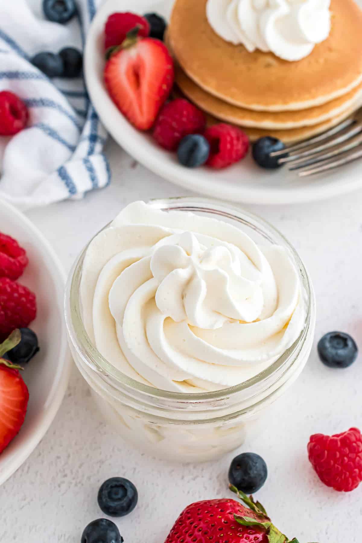 Whipped cream in a small jar, pancakes in background.
