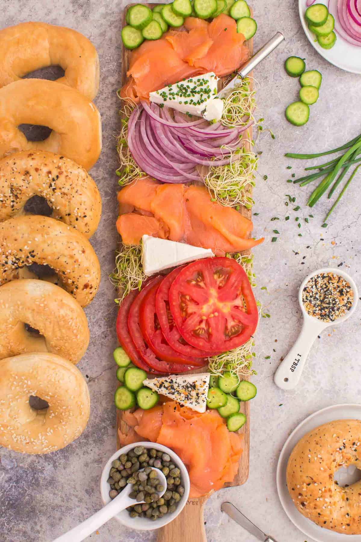 Overhead view of a lox bagel board with many toppings and assorted bagels.