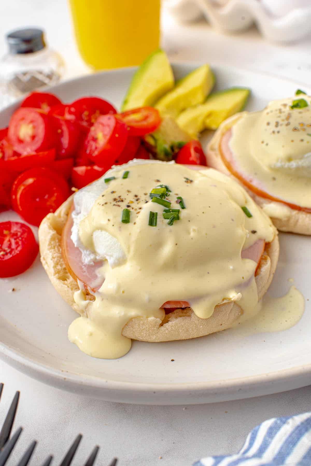 Eggs Benedict on a white plate with tomatoes and avocado.