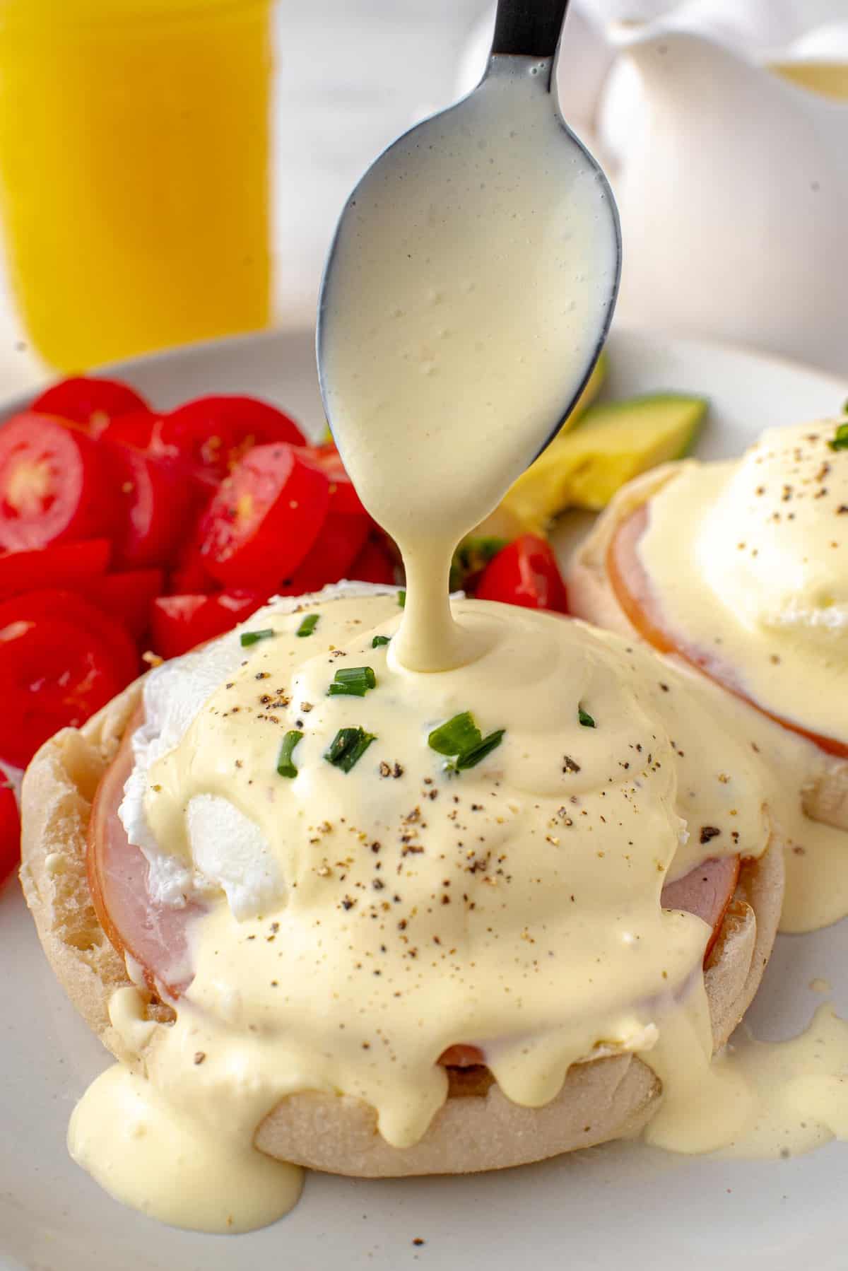 Hollandaise sauce being poured onto eggs, canadian bacon, english muffin.