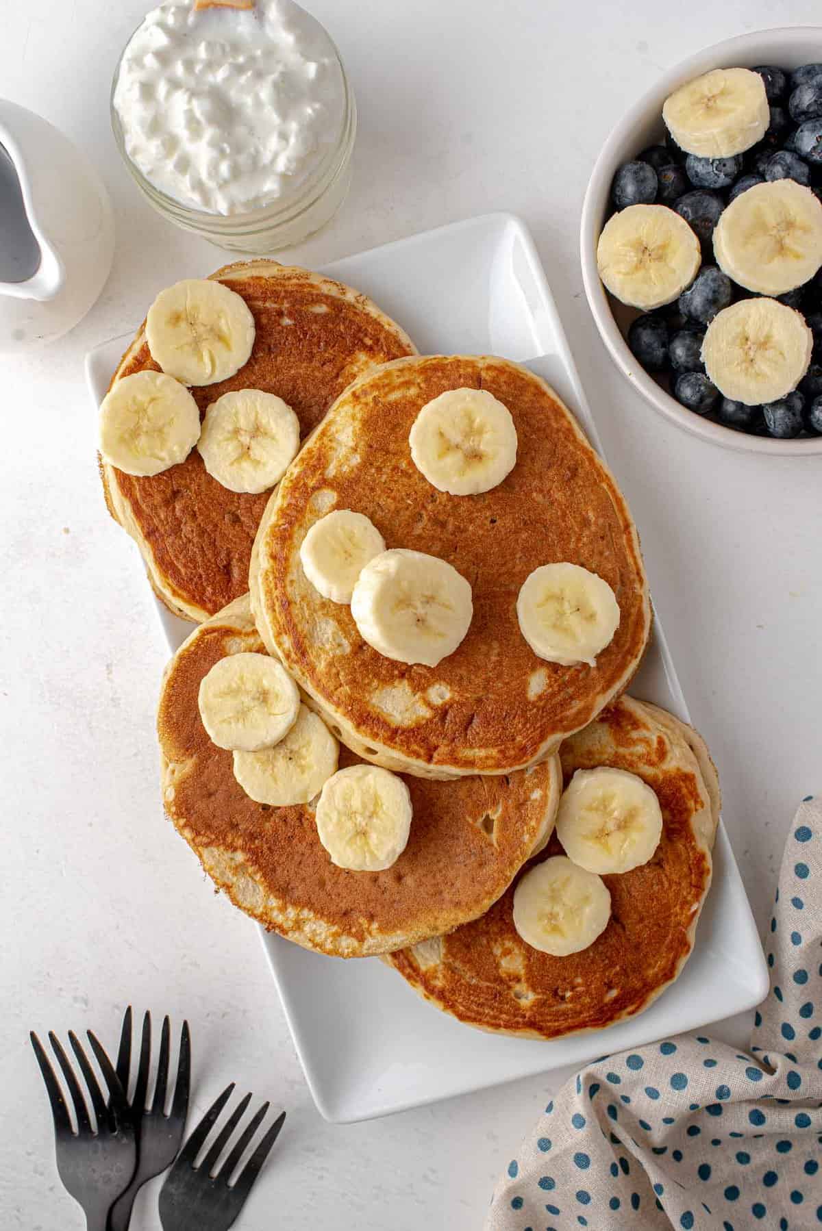 Pancakes on a platter with sliced bananas.