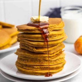 Stack of pumpkin pancakes being drizzled with maple syrup.