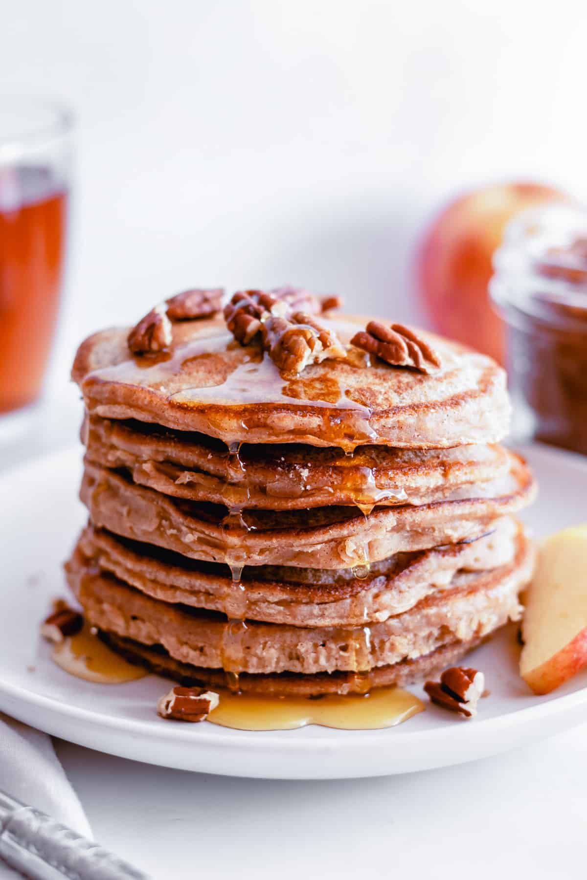 Stack of apple butter pancakes dripping with syrup and topped with pecans.