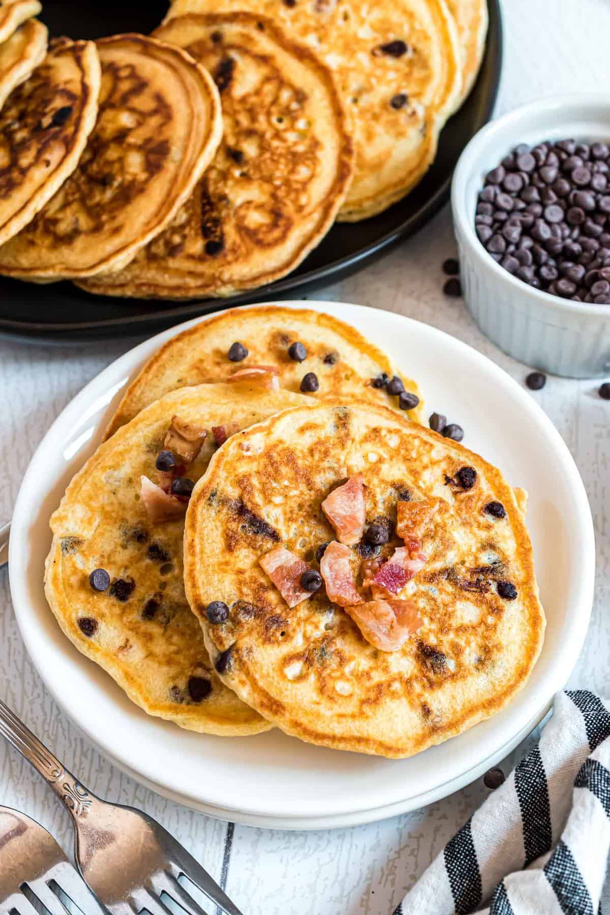 White plate with three bacon chocolate chip pancakes on it. 