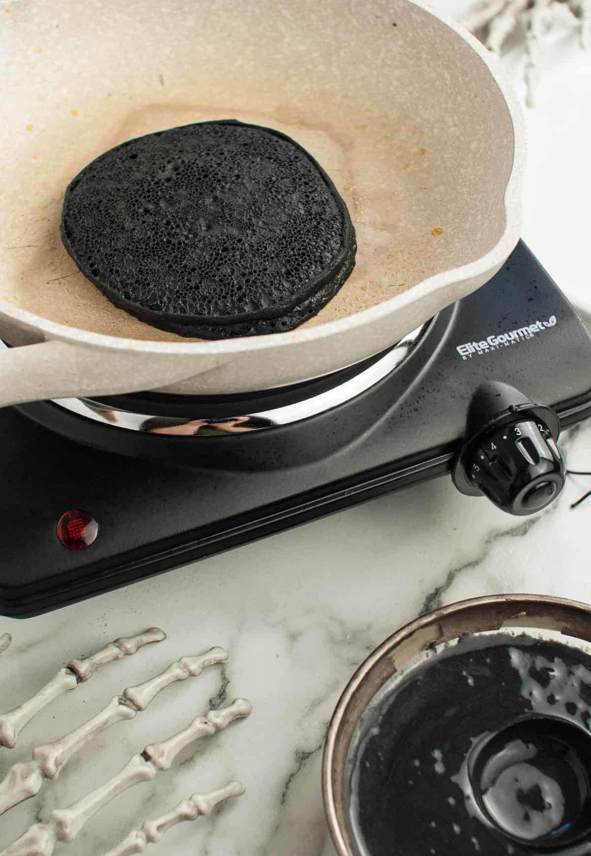 Cooked black pancake in white frying pan.
