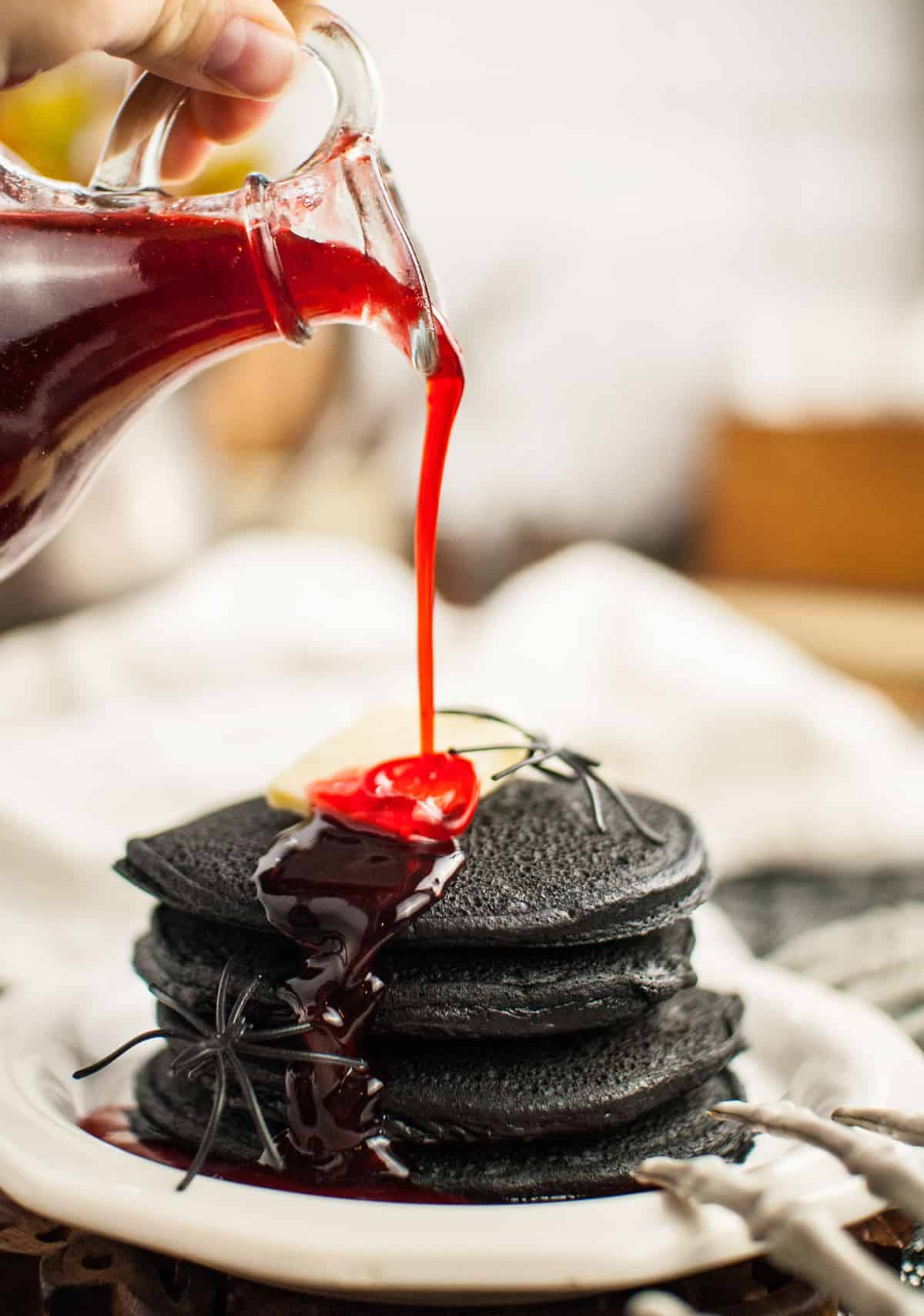 Red syrup being poured on a stack of black pancakes.