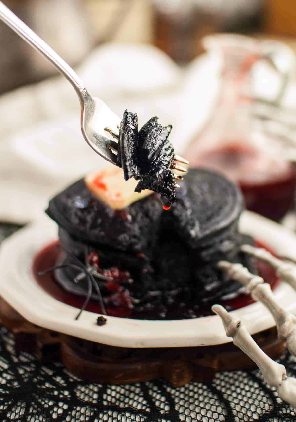 Black pancakes on a fork, a skeleton hand in the foreground.