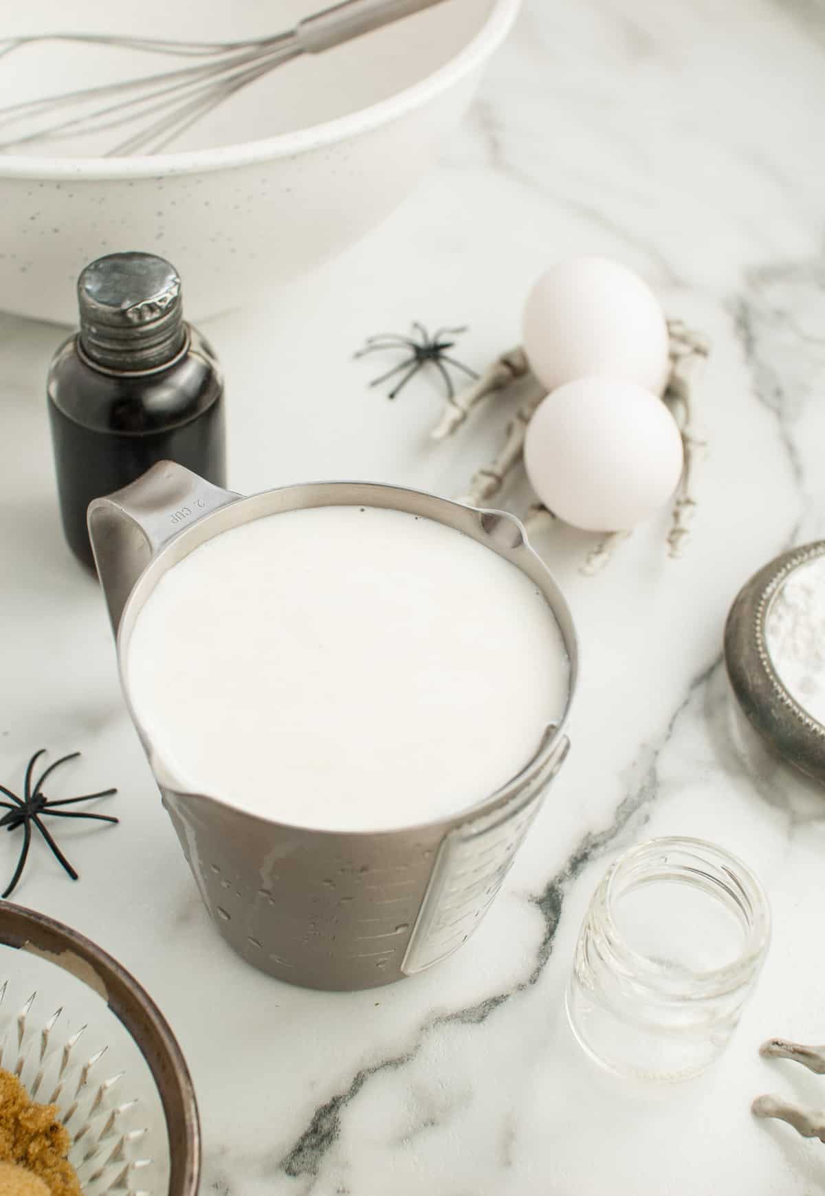 Milk in a metal measuring cup, other ingredients nearby.