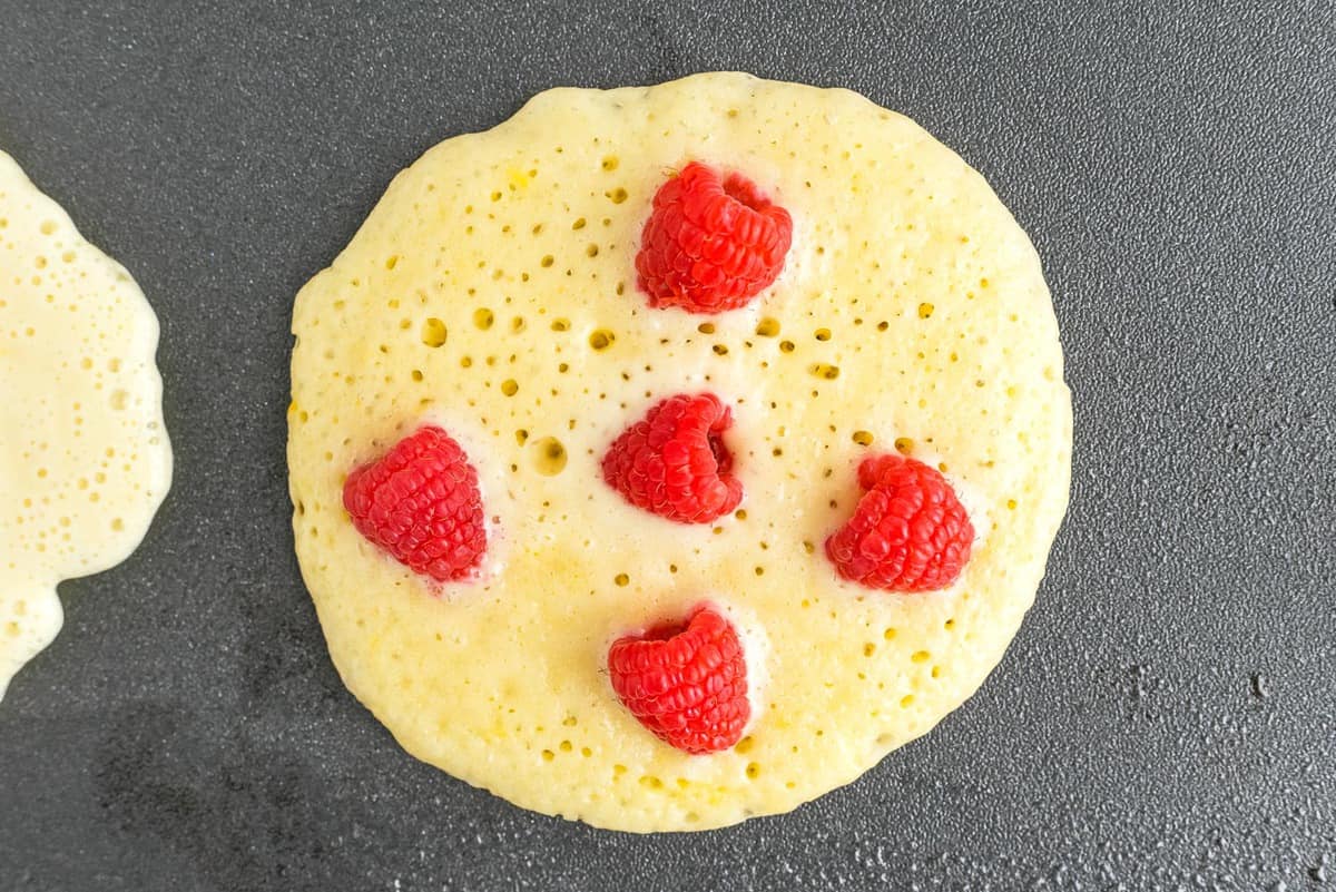 Uncooked pancake topped with fresh raspberries.