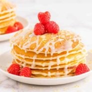 Stack of pancakes topped with fresh raspberries and lemon glaze.