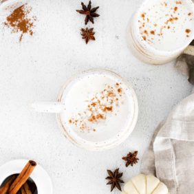 A latte in a white mug on a white background, sprinkled with a spice mixture including cinnamon.