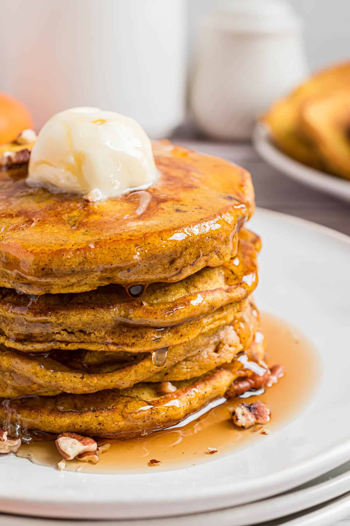 Close up of stack of pumpkin pancakes with a large ball of butter on top and maple syrup.
