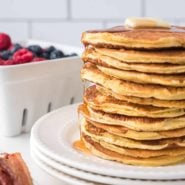 Stack of ricotta pancakes topped with a pat of butter and maple syrup.