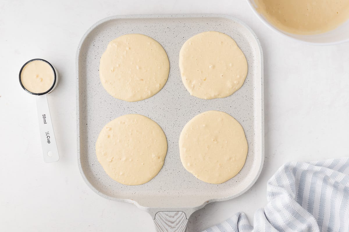 Uncooked pancakes on a white griddle.