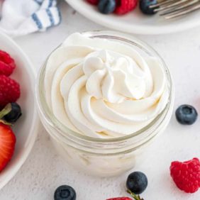 Whipped cream piped into a small jar, berries also visible.