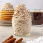 Cinnamon whipped cream in a jar, a stack of pancakes in the background.
