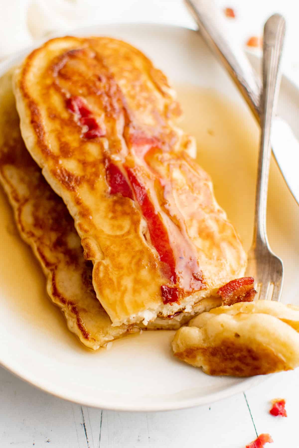 Oval shaped pancakes with a slice of bacon in them, with syrup.