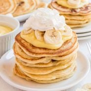 Stack of pancakes topped with pudding, whipped cream, and sliced bananas.