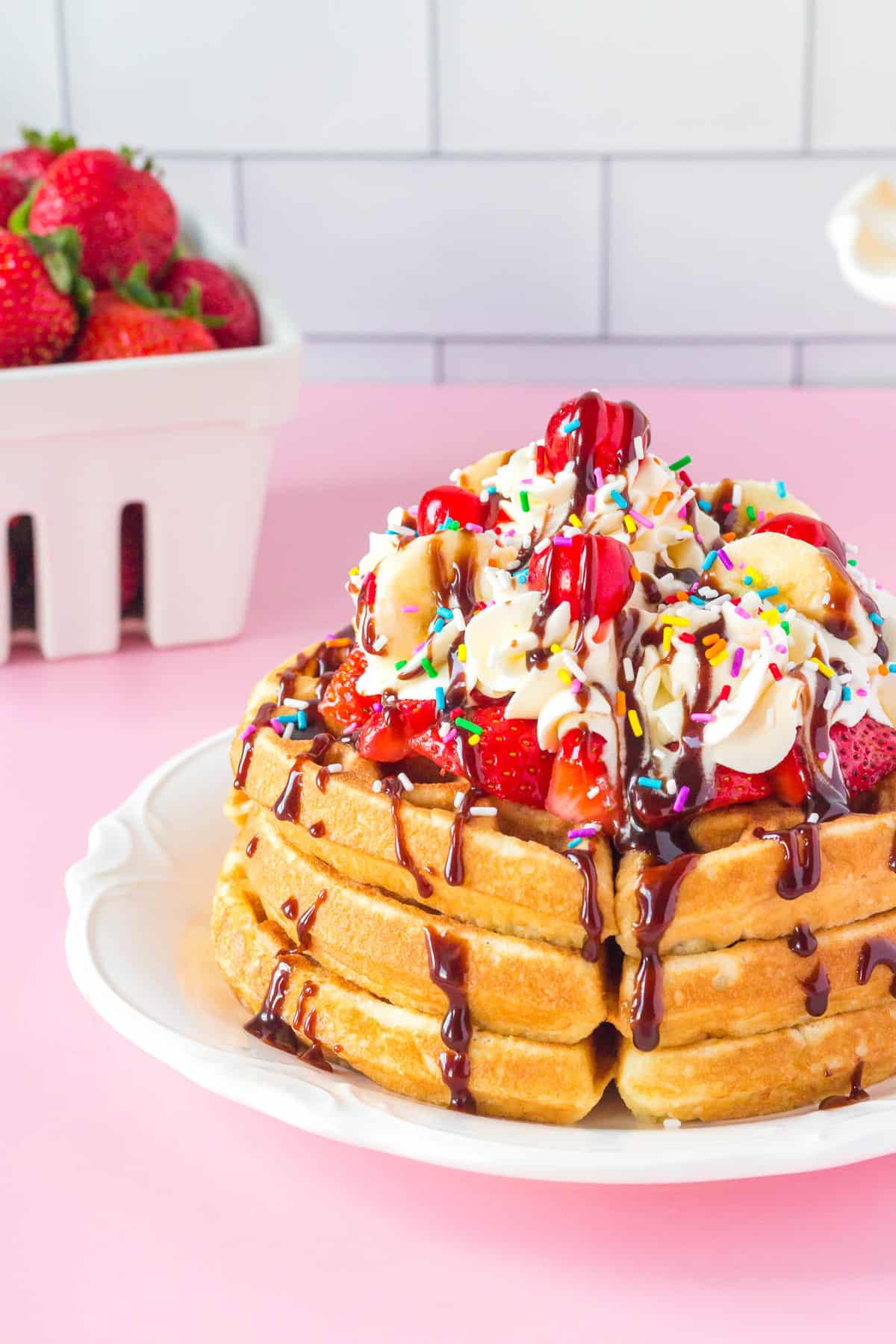 Stack of banana split waffles with whipped cream and toppings.