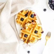 Two small waffles on a white background, topped with blueberries.