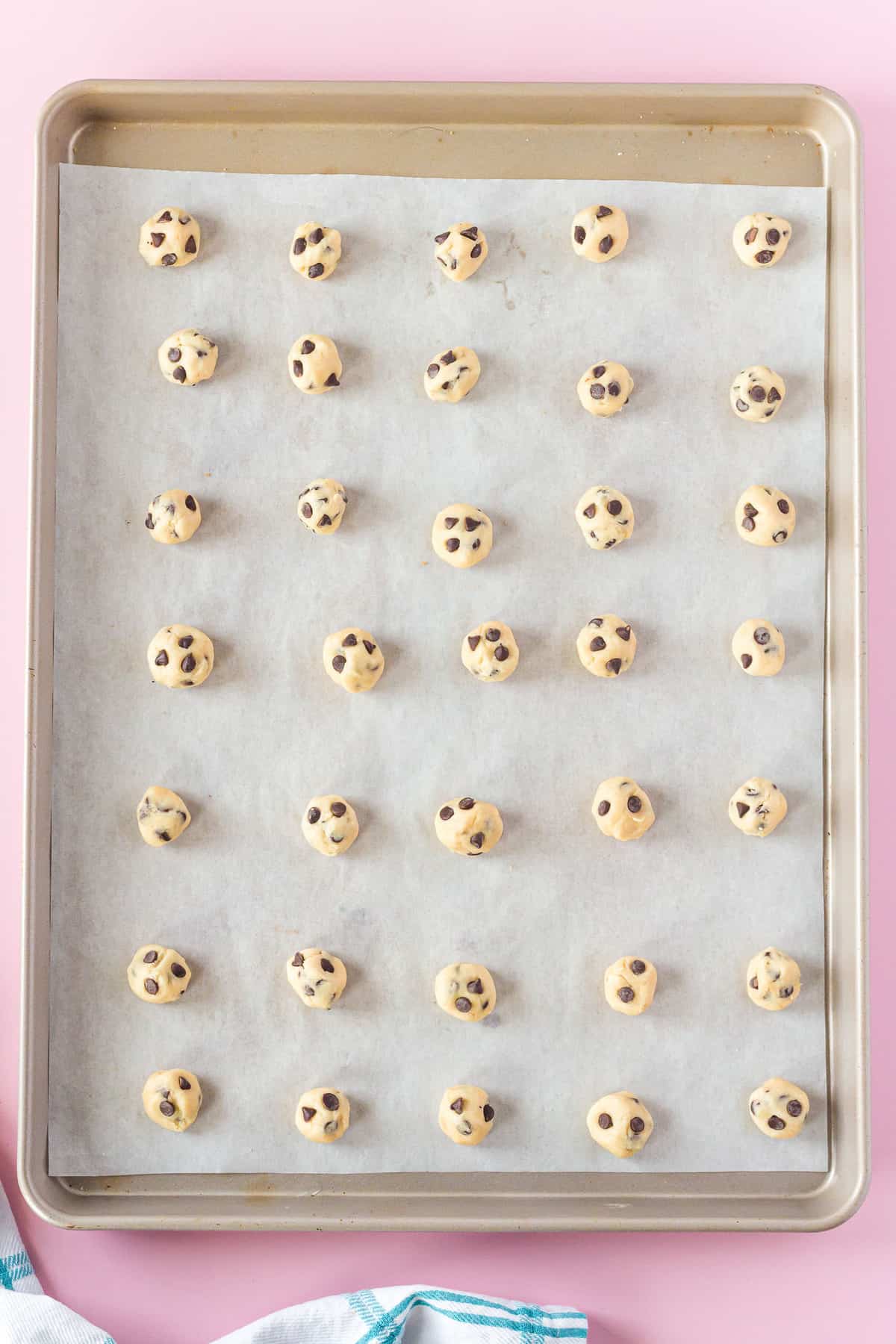 Unbaked mini chocolate chip cookies on a sheet pan.