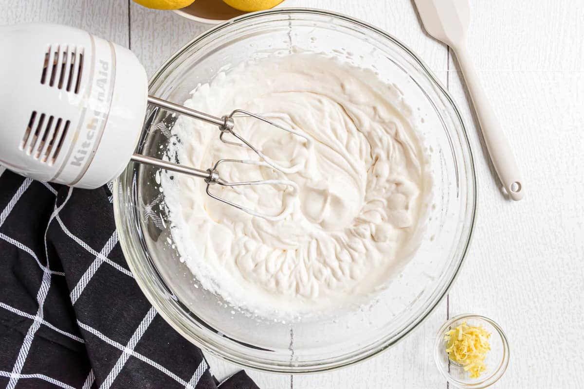 Whipped cream that has been beaten in a clear glass bowl.
