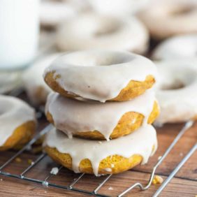 Three pumpkin donuts with white glaze, stacked up on cooling rack.